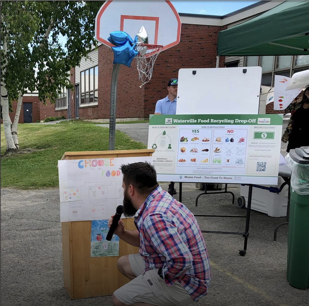 Man kneeling in front of podium, looking at winning Waterville drawing